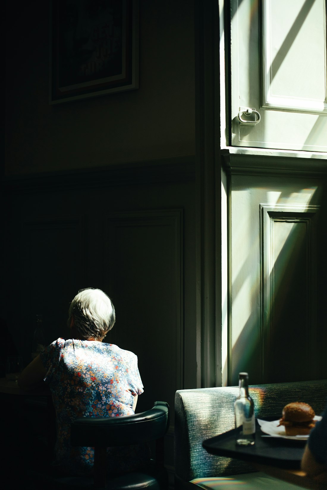Mujer mayor sentada junto a una ventana soleada, con luz cálida