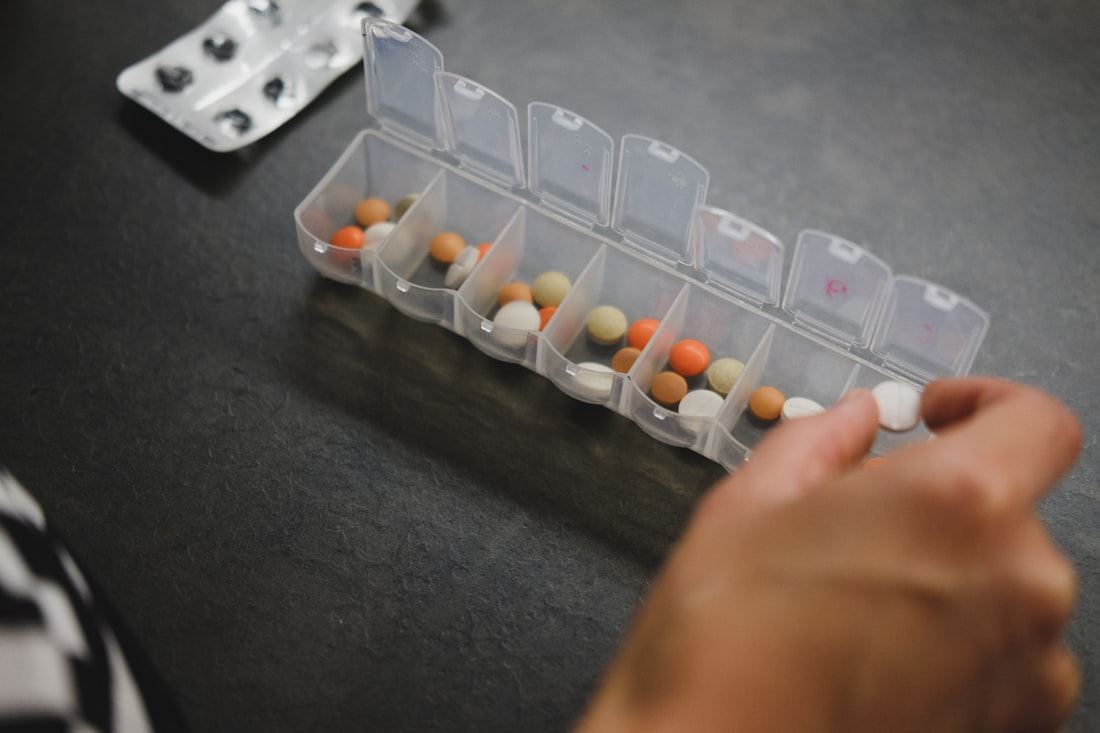 Manos organizando pastillas en un organizador semanal de medicamentos