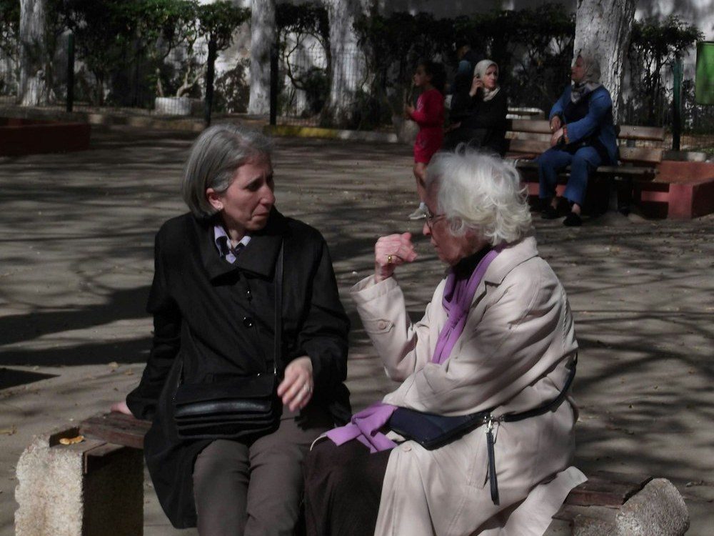 Dos amigas mayores, de cabello cano, conversando juntas al aire libre