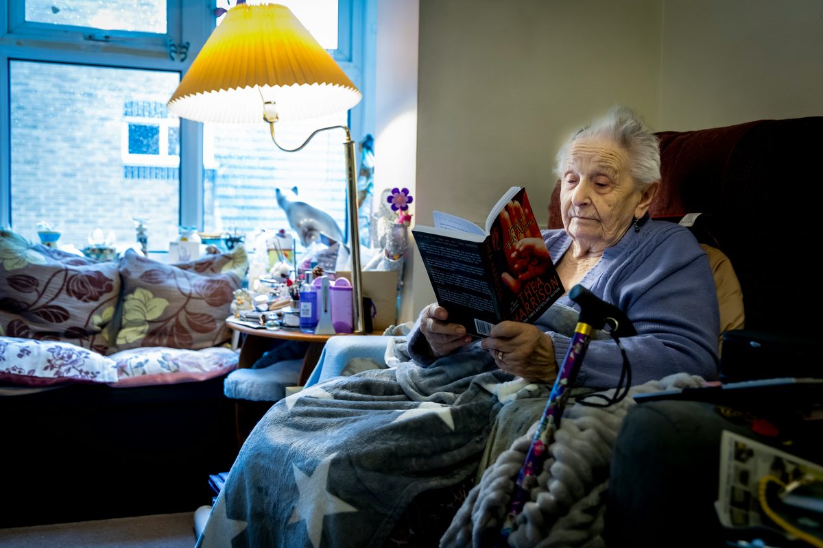 Mujer mayor leyendo tranquilamente en un sillón, con una manta
