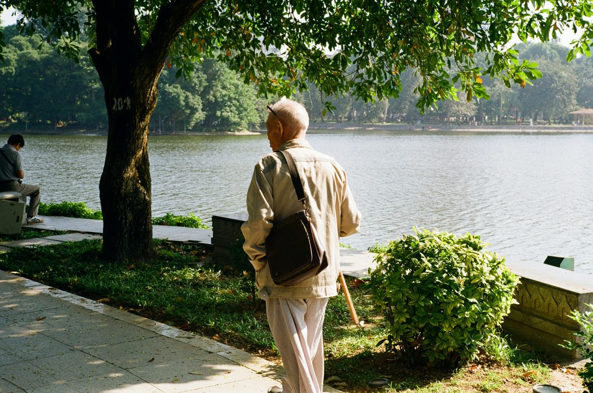Hombre mayor caminando junto a un lago en un parque, con calma