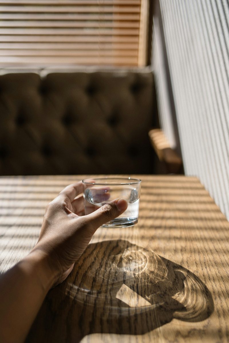 Mano sosteniendo un vaso de agua sobre una mesa de madera con luz cálida