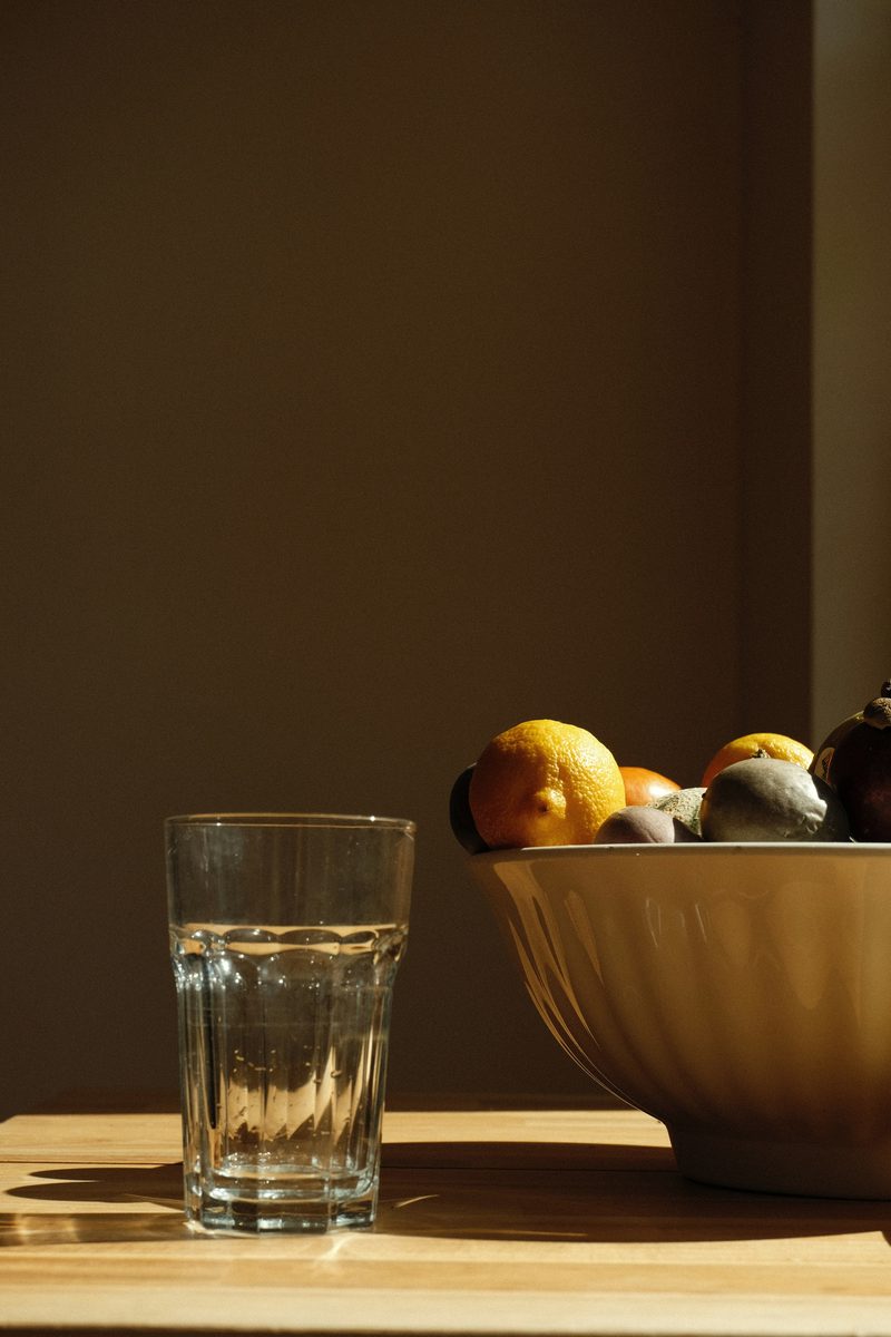 Un tazón de fruta fresca junto a un vaso de agua sobre una mesa de madera