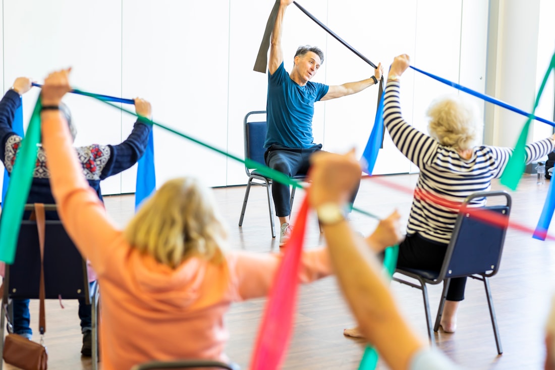 Grupo de personas mayores en una clase de ejercicio guiado, sentadas y de pie, con un instructor