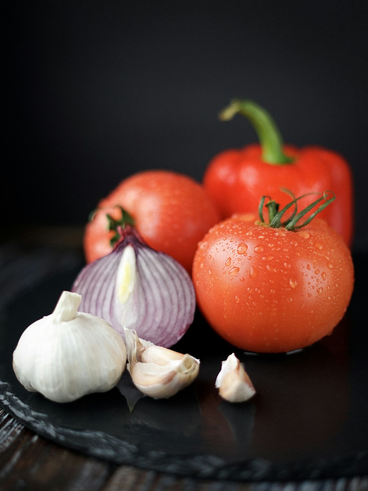 Jitomate, cebolla morada, ajo y pimiento morrón sobre una tabla