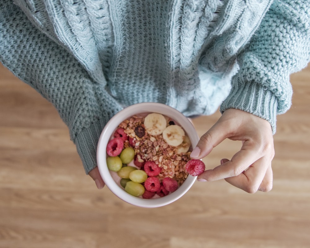 Tazón casero con avena, fruta fresca y granola, sostenido en la mano