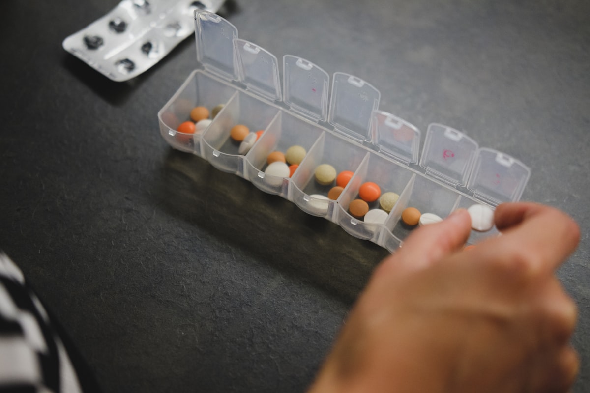 Persona organizando sus medicamentos en un pastillero semanal